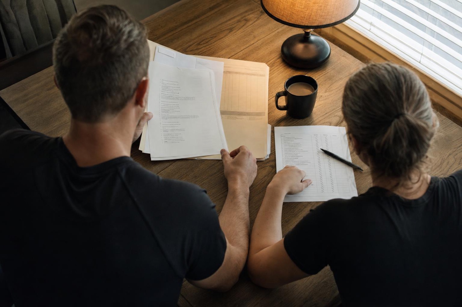 Two pairs of hands reviewing checklists and a manila folder at a table, overhead view